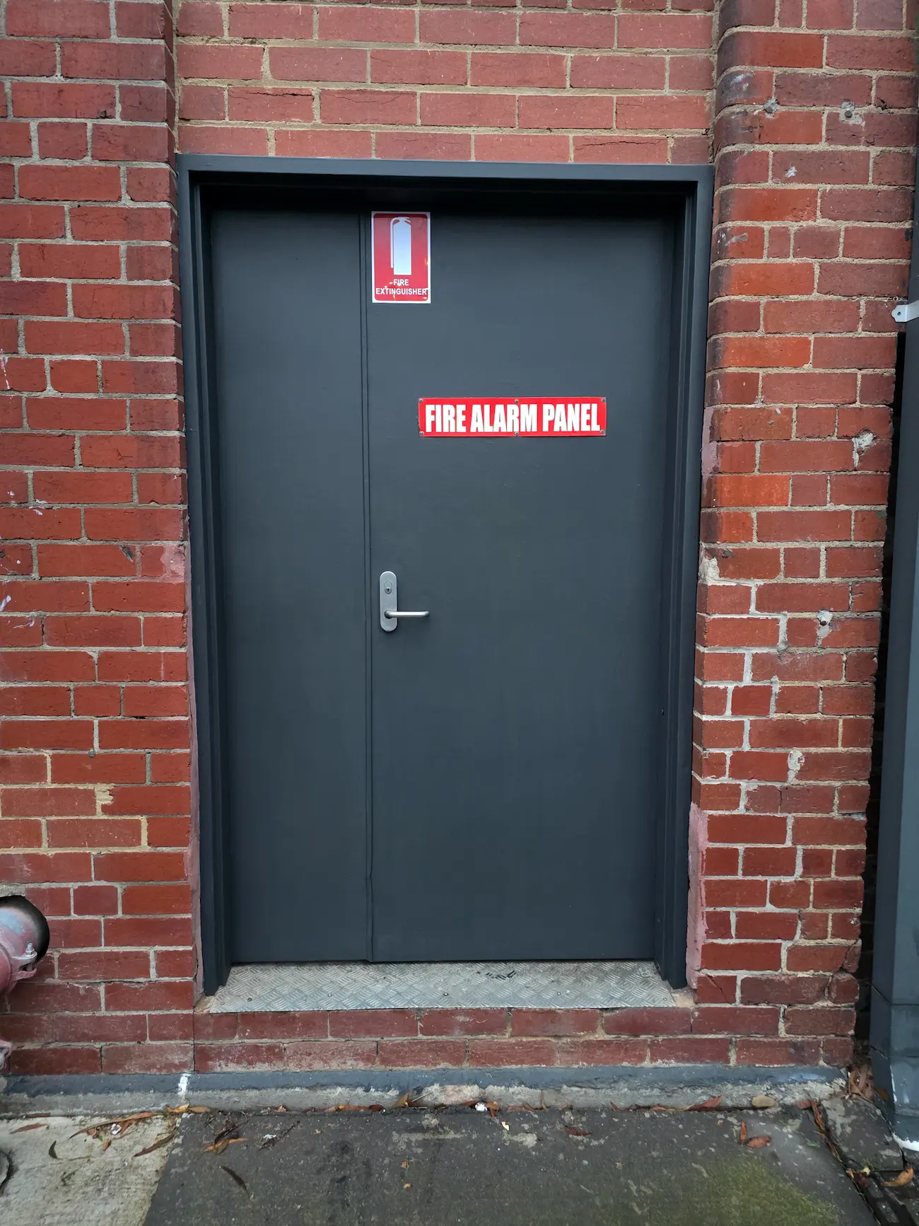 Freshly painted dark service door with fire signage in a brick commercial wall
