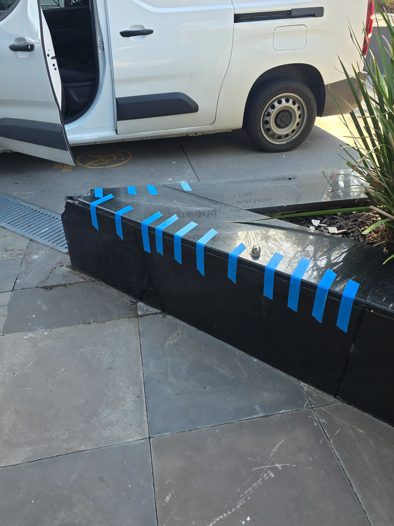 Masked black stone planter edge being repaired at a paved commercial entry