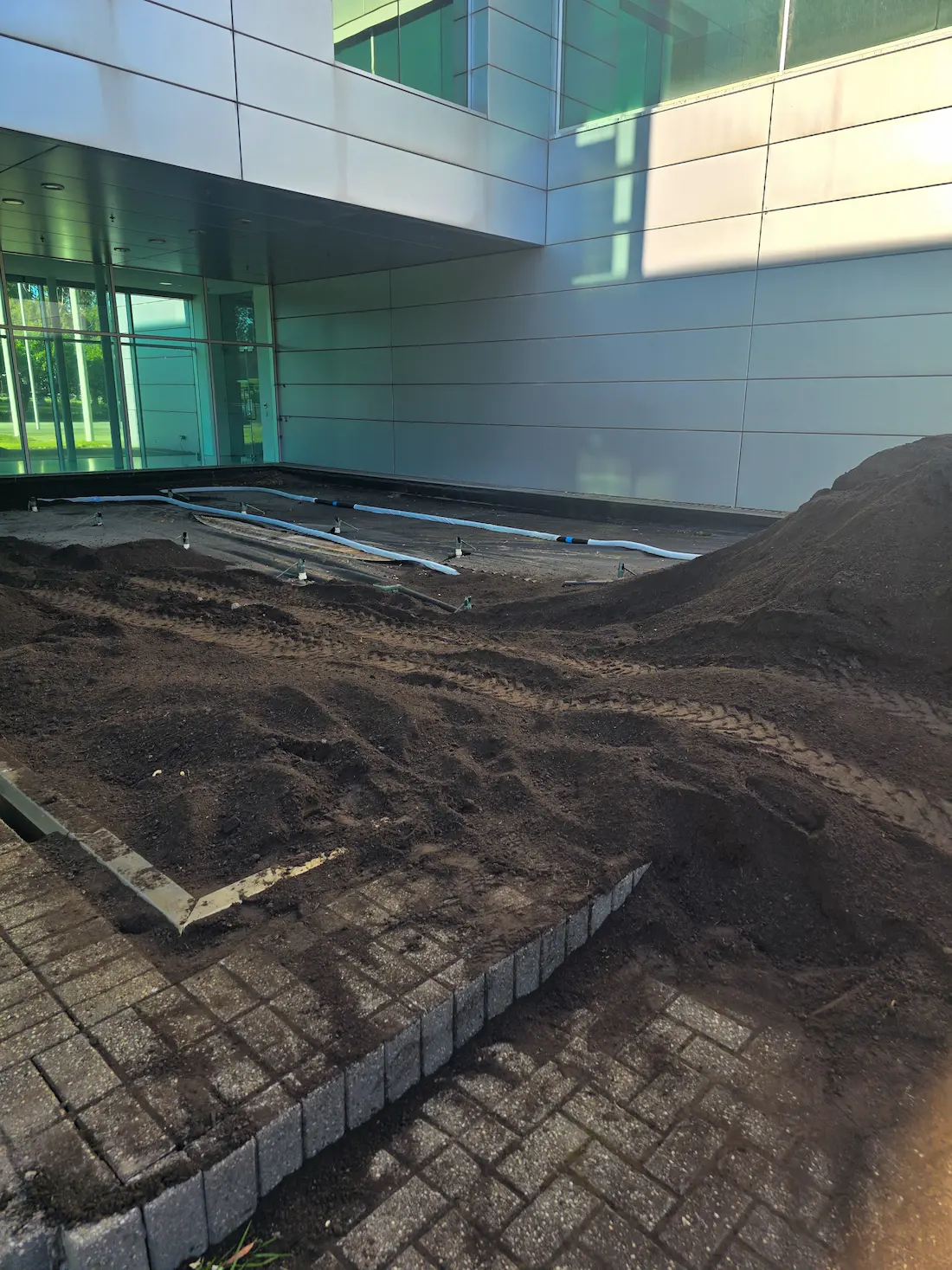 Soil preparation and irrigation lines laid for new garden beds at a commercial building entrance