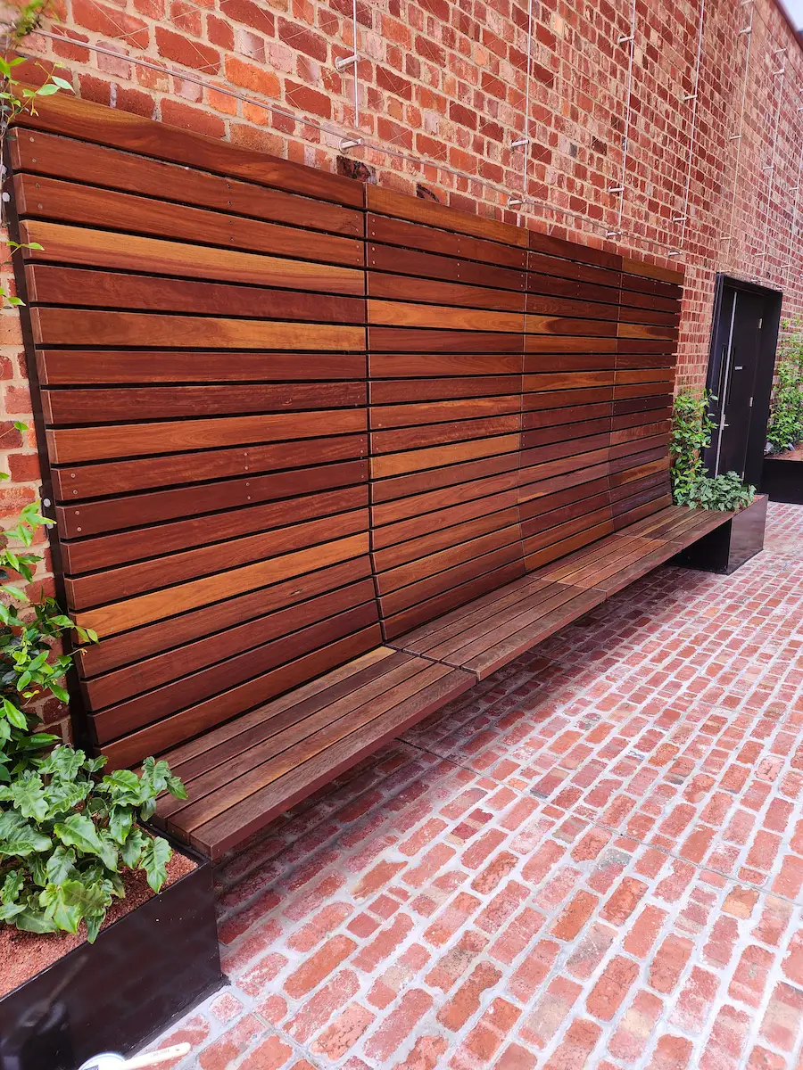 Hardwood batten screen and matching bench seat built against a brick courtyard wall