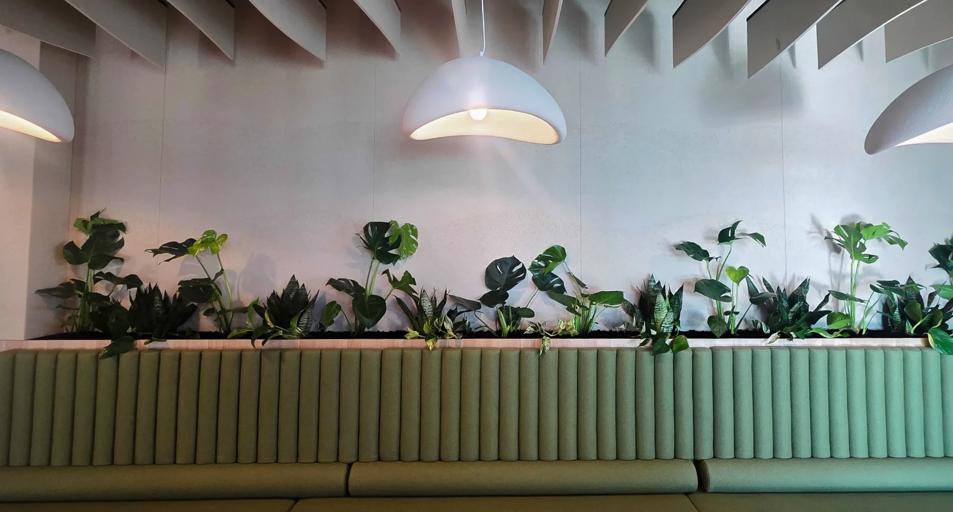 Hospitality interior with a long planter box of tropical plants above a green banquette
