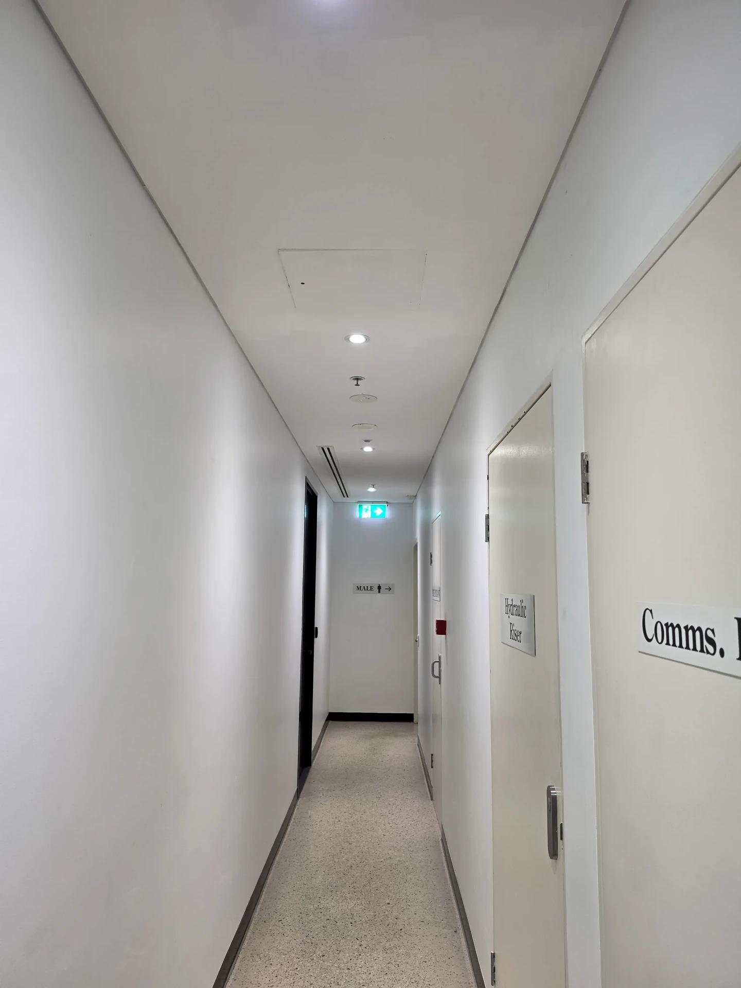Clean white service corridor with signed riser doors and terrazzo flooring