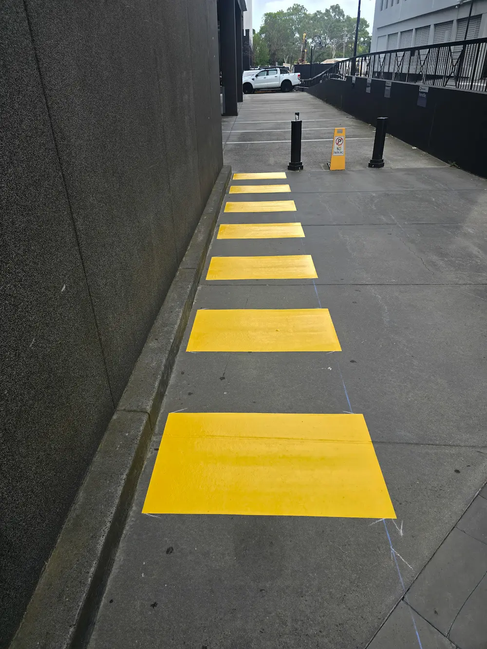 Freshly painted yellow walkway markings along a concrete path beside a commercial building